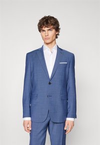 Blauw patteren jasje met notch revers, twee voordoekjes en een enkele knoopsluiting. Draag het over een witte overhemd met kraag.