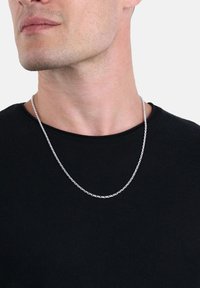 Silverfärgad kedjearmband med en länkdesign, med runda länkar, bärs över en svart t-shirt med rund halsringning. Närbild på nackområdet.