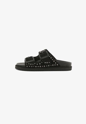 Schwarze Sandale mit Riemen, zwei verstellbaren Schnallen und kleinen silbernen Nieten am oberen Teil, flache Sohle mit strukturierter Unterseite.