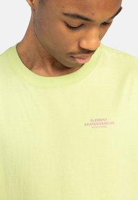 Svetlozelené tričko s krátkym rukávom vyrobené z mäkkého bavlneného materiálu. Na hrudi sa nachádza ružové logo: "ELEMENT SKATEBOARD CO. WORLD WIDE".