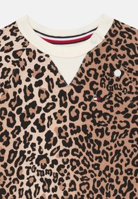Chemise à imprimé léopard beige et noir, dotée d'un col crème côtelé, de boutons et d'un petit logo de marque sur le devant.