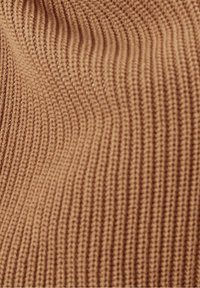 Beige geribbelde gebreide stof met een gladde textuur, voorzien van verticale lijnen en een lichte rek, geschikt voor kleding of accessoires.