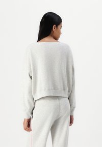 Sweatshirt gris clair avec un large décolleté et un ourlet côtelé, doté de manches longues et d'une coupe courte. Le matériau semble doux et texturé.