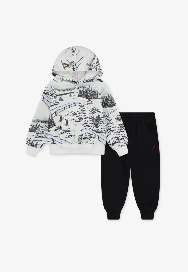 Džemper s kapuljačom s printom zimskog pejzaža u bijeloj boji, s crvenim logotipom; u kombinaciji s crnim trenirkama s elastičnim pojasom.