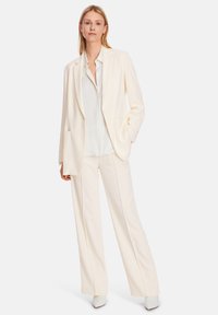White tailored blazer with a single button, paired with matching wide-leg trousers and a light blouse, worn with white pointed shoes.