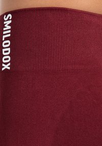 Burgundowa, żebrowana talia z wytłoczonym logo "SMILODOX" w białym kolorze. Miękki, elastyczny materiał z subtelnymi różnicami w fakturze.