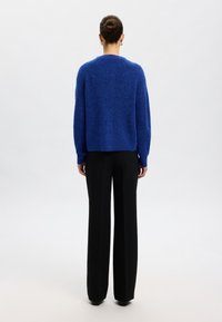 Suéter azul de punto con un corte holgado, puños y dobladillo acanalados. Combinado con pantalones negros de cintura alta, creando un contraste en color y textura.