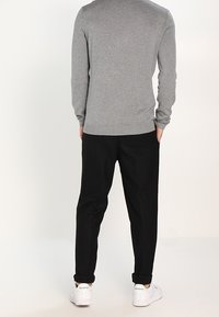 Szary dzianinowy sweter w połączeniu z czarnymi spodniami. Białe trampki z zielonymi akcentami. Skupienie na fakturze i kontrastach kolorystycznych w casualowym ubiorze.