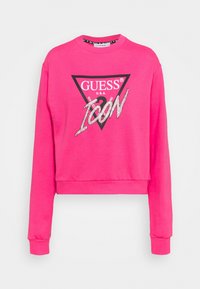 Růžová krátká mikina s dlouhými rukávy. Má černé trojúhelníkové logo s nápisem "GUESS USA" a "ICON" ve stříbrném třpytivém provedení.