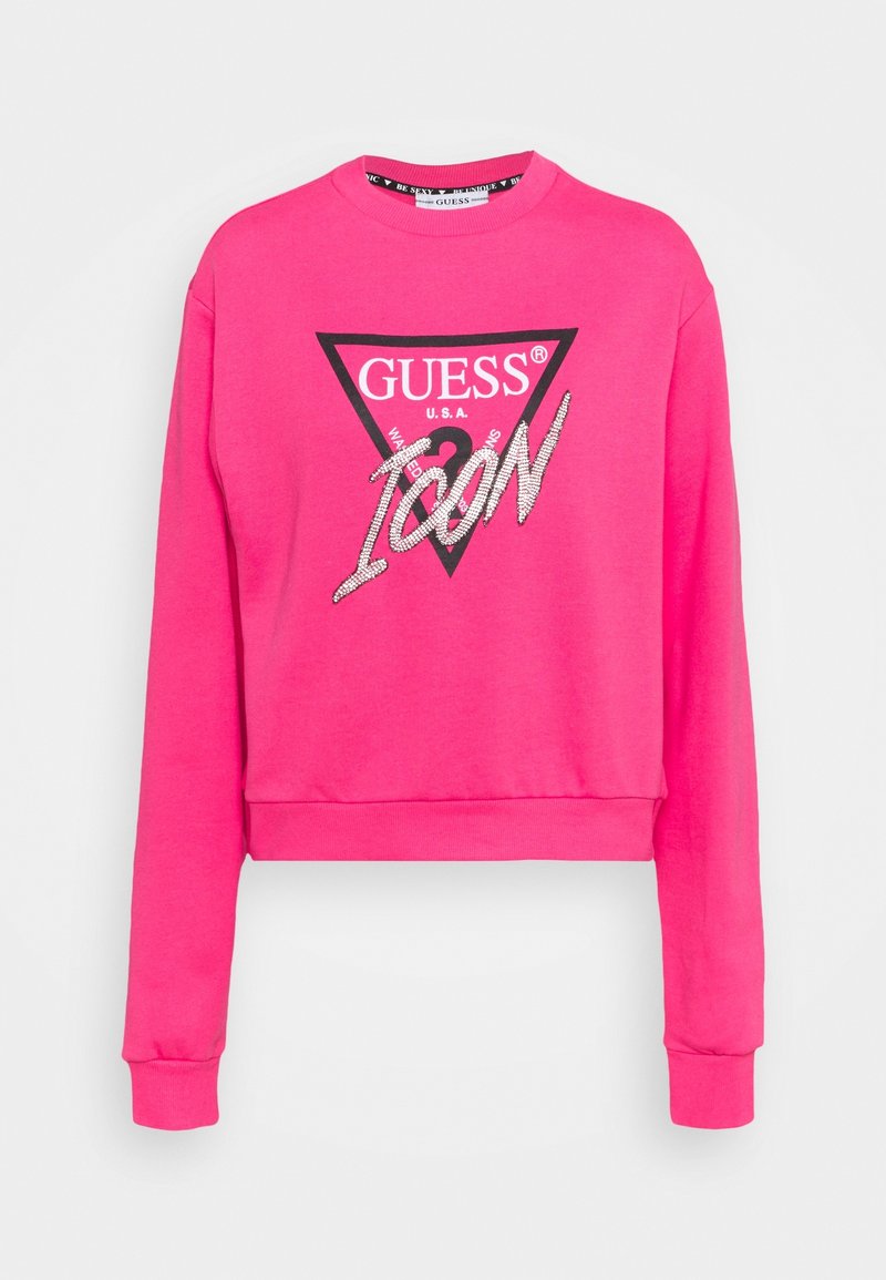 Růžová krátká mikina s dlouhými rukávy. Má černé trojúhelníkové logo s nápisem "GUESS USA" a "ICON" ve stříbrném třpytivém provedení.