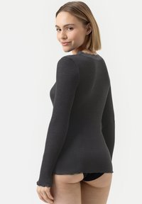 Langarm geribde top in donkergrijs met een golvende halslijn en zoom. Heeft een aansluitende snit en een zachte textuur, gecombineerd met zwarte onderkleding.