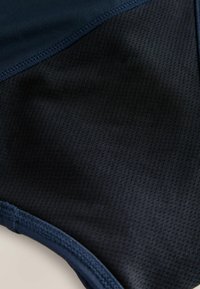 Marineblaue Badebekleidungsstoff mit einem strukturierten Netzmuster, akzentuiert durch glatte Kanten und genähte Nähte, die ein schlankes, sportliches Design präsentieren.