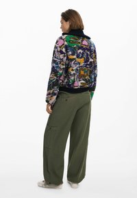 Maglione lavorato a maglia colorato e testurizzato con una vestibilità oversize, caratterizzato da un mix di motivi viola, verde e rosa, abbinato a pantaloni cargo verde oliva.