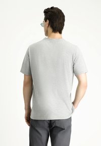 Camiseta gris de manga corta con cuello redondo. Tejido suave y ligero, diseño minimalista y corte recto. Vista trasera que muestra una textura lisa.