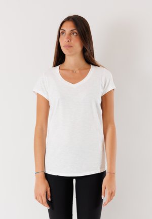 T-shirt bianco a maniche corte con scollatura a V, realizzato in tessuto morbido e leggero. Presenta una vestibilità ampia e una texture delicata. Indossato con pantaloni neri.