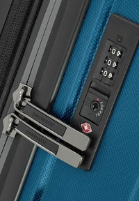 Maleta azul texturizada con doble cremallera plateada unida a un candado de combinación aprobado por la TSA configurado en 0-0-0.