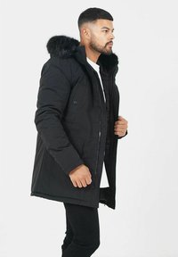 Svart parkajacka med en huva fodrad med päls, dragkedjestängning och två framfickor. Tillverkad av hållbart material med en slät yta.