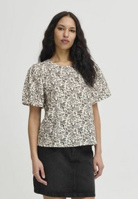 Cremefarbene Bluse mit Blumenmuster, lockeren kurzen Ärmeln und rundem Ausschnitt, kombiniert mit einem schwarzen Jeansrock. Glatte Stofftextur.