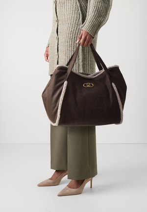 Bolso de viaje de ante marrón con ribete de pelo sintético color crema, detalles en oro y dobles asas. Diseñado con una forma amplia y estructurada.