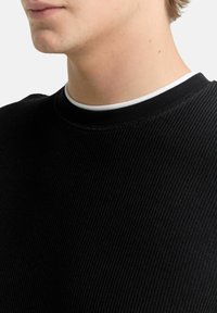 Schwarzes Rippstrick-Sweatshirt mit Rundhalsausschnitt, gefertigt aus texturiertem Stoff und mit einem dezenten weißen Innenkragen, der den Hals- und Schulterbereich betont.