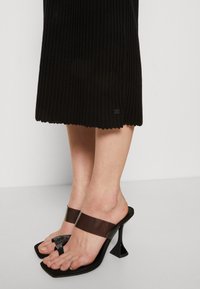 Sandales noires à bout ouvert avec une bride transparente marron et un embout carré. Semelle noire texturée avec un design unique de talon triangulaire.