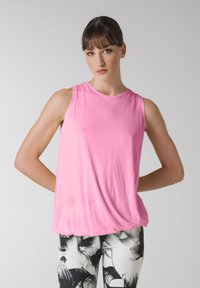 Lyserød ærmeløs top lavet af letvægtsstof, med en rund halsudskæring og en afslappet pasform, parret med sort-hvide mønstrede leggings.