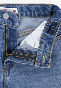 Denim jeans with a light blue wash, featuring yellow stitching, a zip fly, button closure, and a back pocket with decorative stitching.