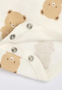 Bavlněná kojenecká kombinéza s světle krémovou látkou a vzorem hnědých medvědů. Zapínání na cvočky na spodní části s lesklými stříbrnými doplňky.