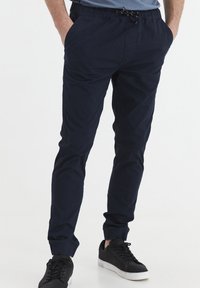 Navy blue jogger pants with an elastic waistband and adjustable drawstring, featuring side pockets and tapered cuffs. Soft fabric texture.