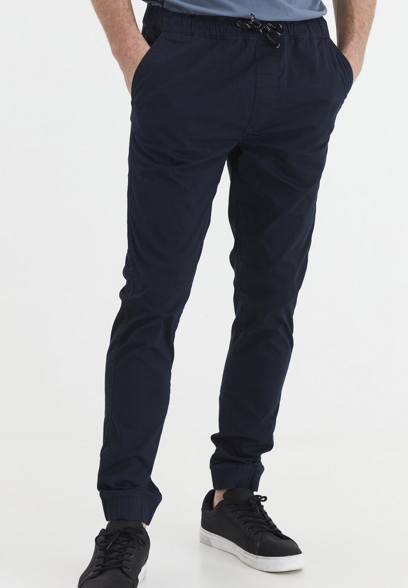 Navy blue jogger pants with an elastic waistband and adjustable drawstring, featuring side pockets and tapered cuffs. Soft fabric texture.