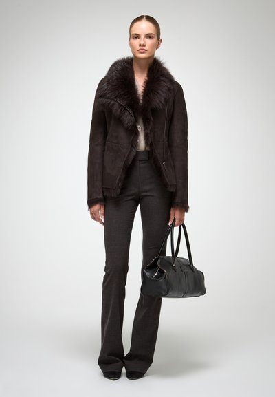 Chaqueta de ante marrón oscuro con cuello de piel sintética, combinada con pantalones gris de campana y un bolso de cuero negro, que presenta acentos de herrajes plateados.