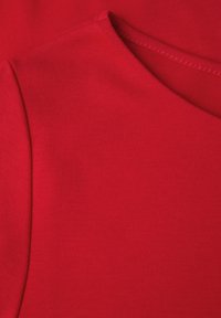 Rode katoenen stof met een gladde textuur, voorzien van een ronde halslijn en een eenvoudig ontwerp, met de nadruk op strakke lijnen en minimale details.