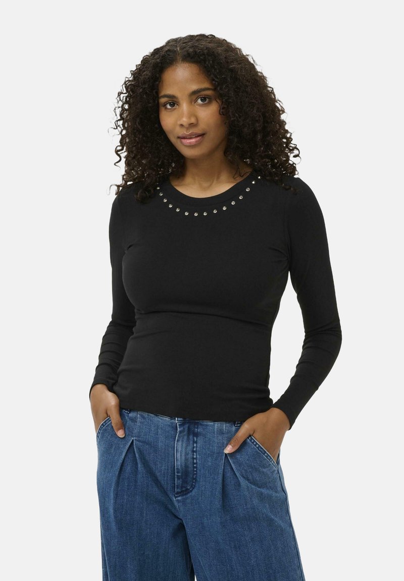 Bluză neagră cu mâneci lungi, având un guler rotund decorat cu năsturei argintii, asociată cu o pereche de pantaloni din denim deschis la culoare, lejeri.