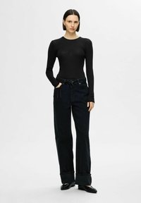 Svart ribbad långärmad topp i kombination med hög midja mörka jeans med lös passform och uppvikta ben, fulländat med enkla svarta skor.