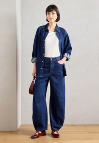 Τζιν πουκάμισο και φαρδιές τζιν παντελόνες σε σκούρο μπλε, με λευκό τοπ από κάτω. Κόκκινα γυαλιστερά παπούτσια και καφέ τσάντα ολοκληρώνουν το σύνολο.