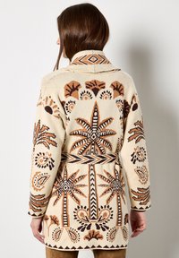 Kremowy kardigan z misternymi brązowymi i czarnymi wzorami palm i paisley, z paskiem w talii oraz kołnierzem typu szal.