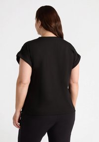 Schwarzes kurzärmliges Oberteil aus glattem Stoff mit umgeschlagenen Ärmeln; lässige Passform und einfaches Design. Keine sichtbaren Muster oder Hardware-Details.