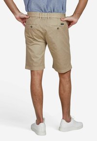 Beige katoenen shorts met een elastische tailleband, achterzakken met knoopsluitingen en omgeslagen zoom. Gecombineerd met witte sneakers.