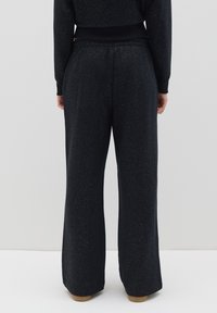 Schwarze weite Hosen aus weichem Material mit subtiler Glitzerstruktur, ausgestattet mit einem elastischen Bund und tapered Bündchen.