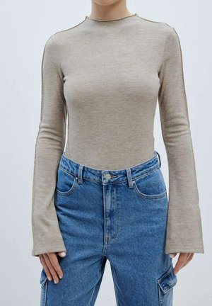 T-shirt beige clair à manches longues avec un design ajusté et un col rond, associé à un jean en denim bleu taille haute avec une poche avant.