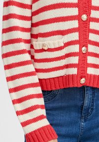 Cardigan a strisce rosse e crema con orlo a coste, grandi bottoni e dettaglio tasca. Realizzato in tessuto lavorato a maglia, presenta un aspetto texture.
