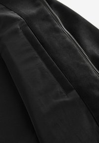 Schwarze Jacke mit strukturiertem Oberfläche und glattem Stoff. Verfügt über einen kontrastierenden Reißverschluss, elegante Linien und dezente Taschendetails.
