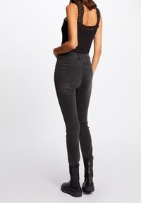 Czarny bodysuit z koronkowymi wykończeniami, w połączeniu z szarymi, dopasowanymi dżinsami z tylnymi kieszeniami i długością do kostek, uzupełniony czarnymi botkami.