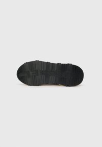 Black rubber sneaker sole with pronounced tread pattern and branding. Textured surface with ridges and depressions for grip.