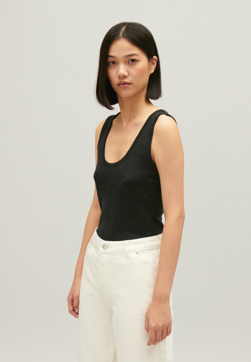 Zwarte mouwloze tanktop met een ronde hals, gemaakt van gebreide stof, gecombineerd met hoge witte broeken. Gladde textuur, nauwsluitende pasvorm.