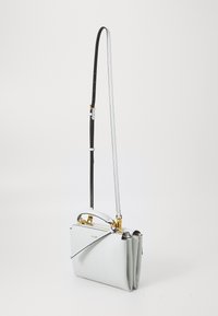 Sac bandoulière blanc en cuir compact avec quincaillerie dorée, une sangle noire réglable et un design unique plié. Texture lisse et forme structurée.