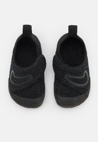 Svarta slip-on-skor med vävd textur, rundad form och svarta gummisulor. Har en framträdande svart logotyp på ovansidan.