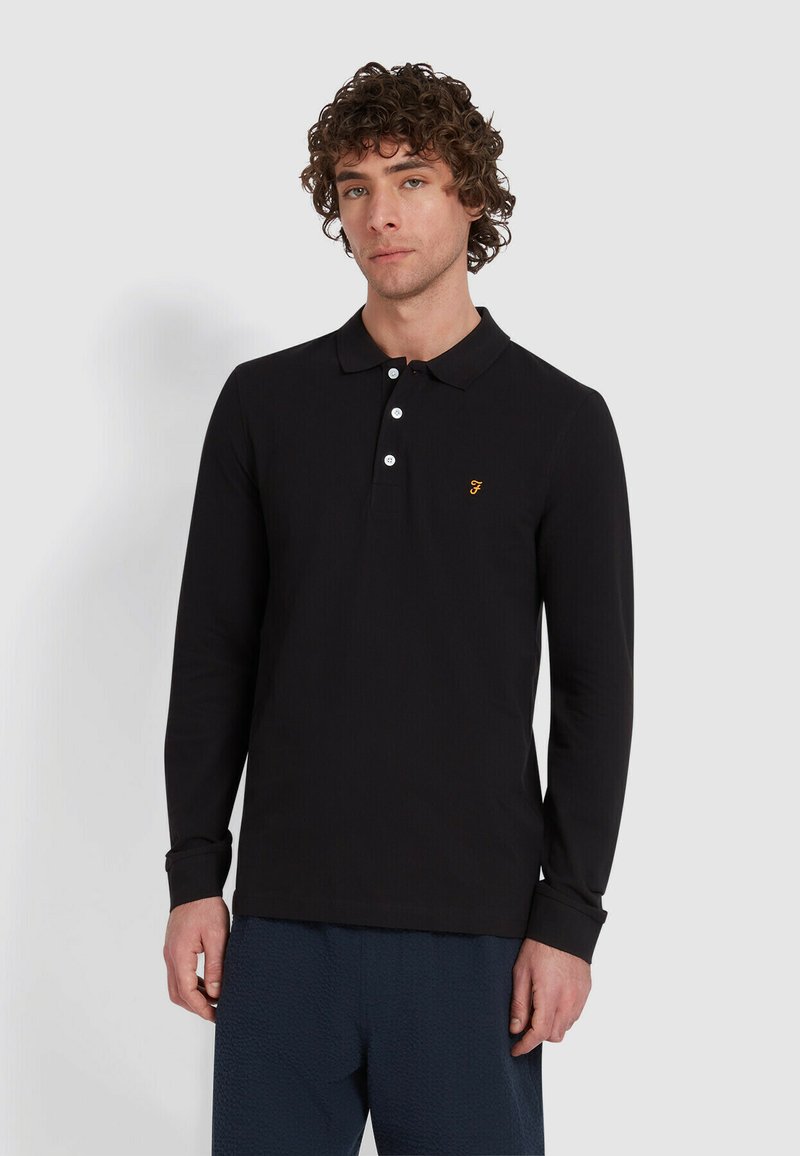 Zwarte lange mouwen polo shirt met een kraag, voorzien van een drieknoopsluiting en een geborduurd geel logo op de linker borst. Gestructureerde stof.