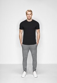 Sort kortærmet t-shirt, grå sweatpants og hvide sneakers. T-shirten har et enkelt design, mens sweatpantsene er tapered med manchetter.