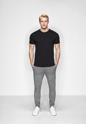 Sort kortærmet t-shirt, grå sweatpants og hvide sneakers. T-shirten har et enkelt design, mens sweatpantsene er tapered med manchetter.